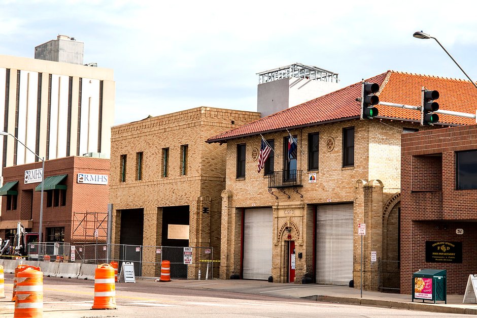 commercial building located in a city. the building features tan bricks and a red roof and garage doors. there are traffic cones around the building